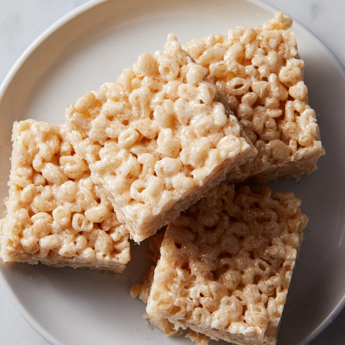 Golden Rice Krispie Treats, glistening with melted marshmallow, stacked neatly on a plate.