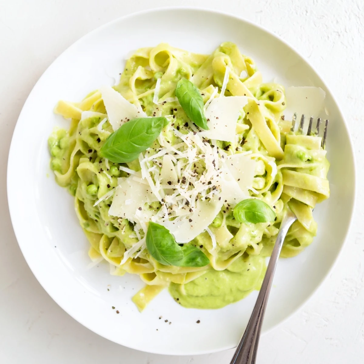 Overhead view of a serving of Creamy Green Pea Alfredo, garnished with fresh basil and grated Parmesan cheese.