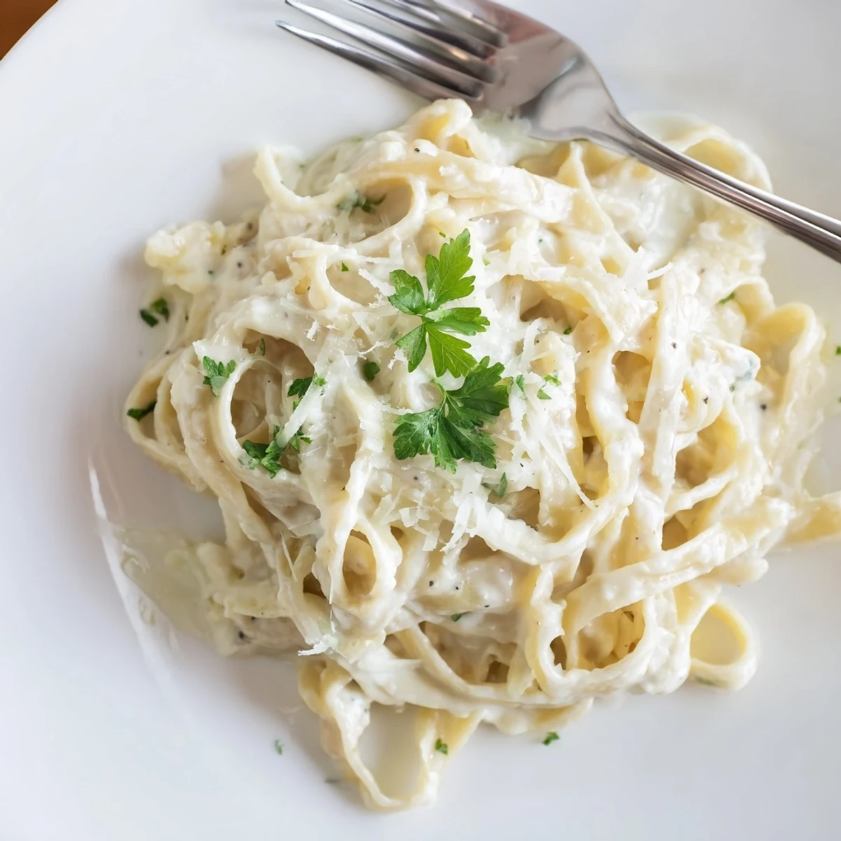 Creamy Easy Creamy Cauliflower Alfredo pasta twirls on a white plate, garnished with parsley and fresh Parmesan.