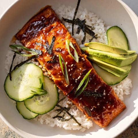 A close-up of a colorful Emily Mariko-Inspired Sticky Orange Gochujang Salmon Bowl with sesame seeds and nori.