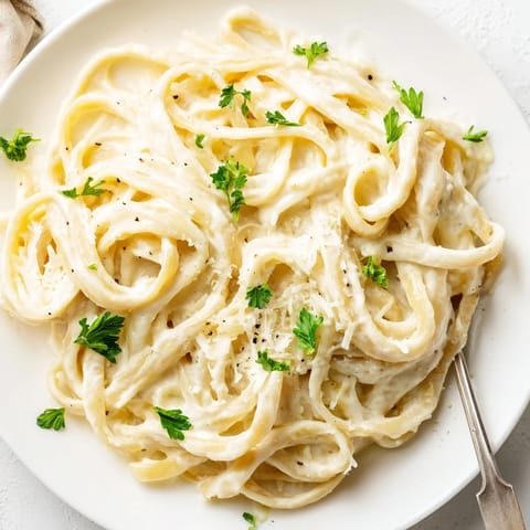 A bowl of Easy Creamy Cauliflower Alfredo shows velvety sauce clinging to fettuccine, with steam rising.