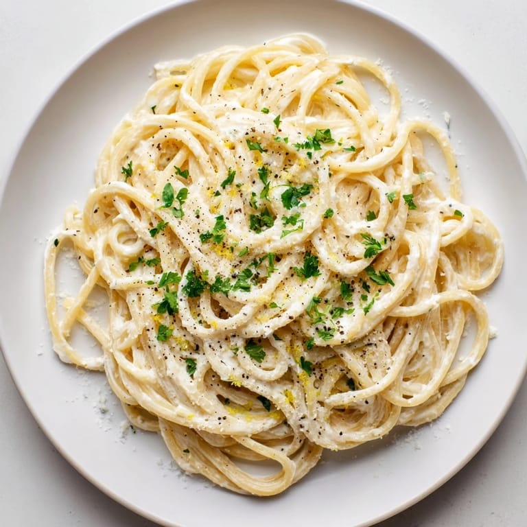 A close-up of Lemon Ricotta Pasta on a rustic board, showing creamy ricotta sauce clinging to al dente spaghetti and a wedge of lemon.  