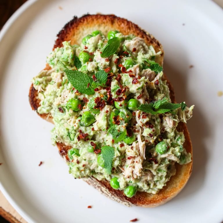 Rustic bread slice holding a hearty mix of smashed green peas, shredded chicken, and spicy chili flakes, perfect for a quick lunch.